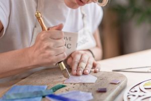 Artist,cutting,sheets,of,stained,glass,into,small,mosaic,squares.